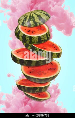 Ripe watermelon cut into pieces flying in the air, with a pink paint splash. Floating, flying, levitating sliced fresh watermelon with splash of water Stock Photo