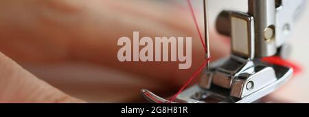 Hands pulling red thread in sewing machine needle Stock Photo
