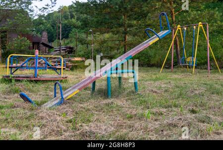 Old swings, abandoned playground equipment, on the background of swings and carousels. Stock Photo
