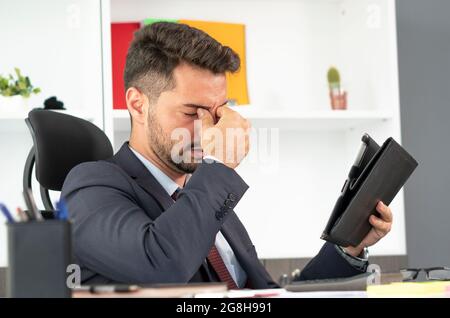 Portrait of tired man working with digital tablet overtime alone in office , closing eyes and pinching his nose trying to relieve stress. Stock Photo