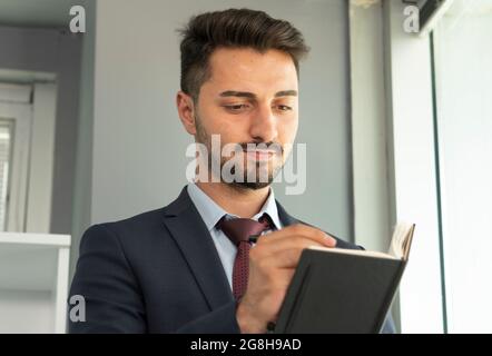Portrait of concentrated business person in suit writing down his plans to notepad. Stock Photo
