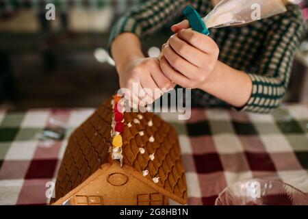 young girl using icing to decorate gingerbread house Stock Photo