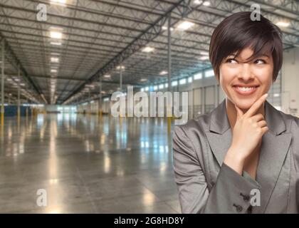 Thinking Mixed Race Businesswoman Standing in Empty Industrial Warehouse. Stock Photo