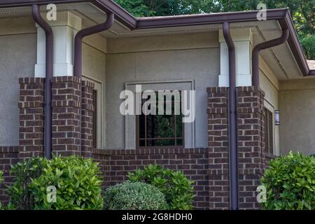 Close up vintage style brick facade brown gutters and beautiful green landscaped bushes Stock Photo