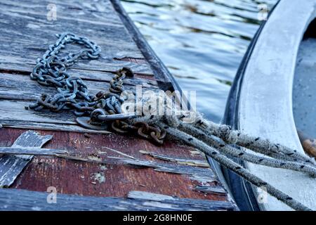 Old wooden boat with peeled paint, tied with rope and rusty chain with padlock on a wooden dais next to the lake. horizontal Stock Photo