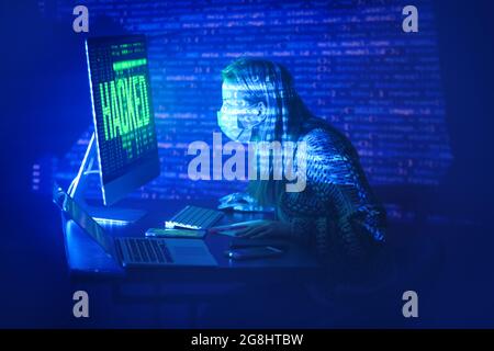Woman sitting near hacked computer in dark room Stock Photo