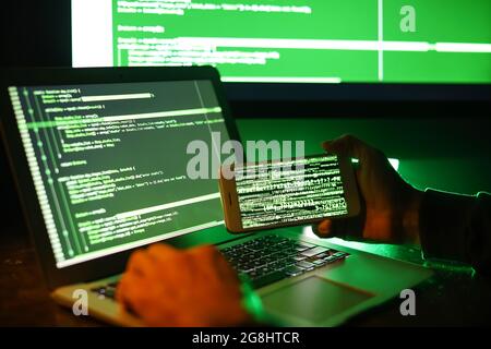 Hacker with mobile phone using computer in dark room Stock Photo