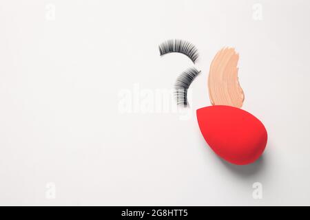 Makeup sponge with sample of tonal foundation and false eyelashes on white background Stock Photo