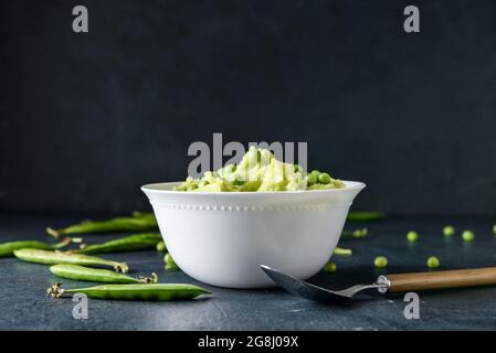 Bowl with mashed potatoes and green peas on dark color background Stock Photo