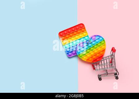 Pop it fidget toys and shopping cart on color background Stock Photo