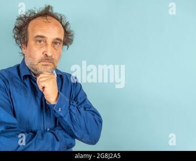 skeptical looking man mad scientist type with blue man shirt and wild hair against light blue background Stock Photo