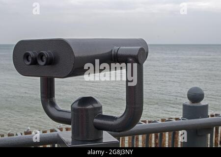 Shiny black binoculars on a swivel hinge on observation deck on sea embankment, directed to the right at horizon with azure sea and cloudy sky below i Stock Photo