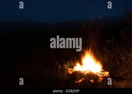 Night view with a beautiful campfire flame and sparks against the background of snowy mountains, shot at long exposure Stock Photo