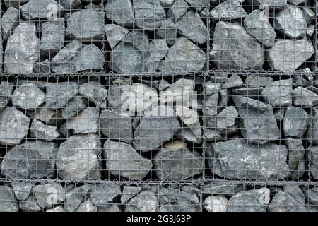 The texture of a fence made of many gray stones, reinforced with a metal mesh. Background. Stock Photo