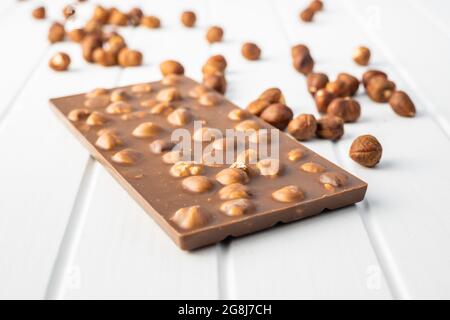Chocolate bar with hazelnuts on white table. Stock Photo