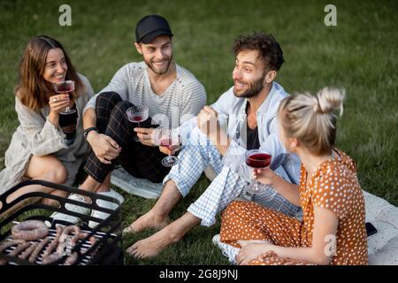 Friends sitting together at the picnic with barbeque and wine Stock Photo