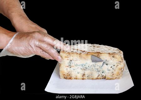 hands cut a large piece of stilton cheese. Isolated on a black background. Stock Photo