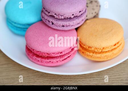 Macaroons in a white plate close up, colorful sweets. Strawberry, blueberry, vanilla and orange almond cookies with filling on a table Stock Photo