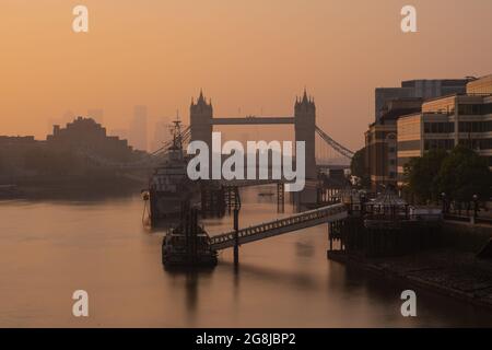 City of London, UK. 21st July, 2021.UK Weather:  Beautiful hazy sunrise over Tower Bridge, The City of London and HMS Belfast as the capital wakes up to another day of glorious sunshine and clear skies during the heatwave. Credit: Celia McMahon/Alamy Live News Stock Photo