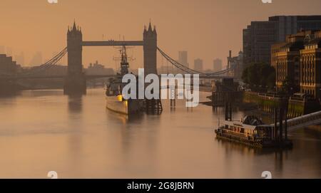 City of London, UK. 21st July, 2021.UK Weather:  Beautiful hazy sunrise over Tower Bridge, The City of London and HMS Belfast as the capital wakes up to another day of glorious sunshine and clear skies during the heatwave. Credit: Celia McMahon/Alamy Live News Stock Photo