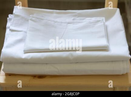 A set of white bed linen is lying on a chair Stock Photo