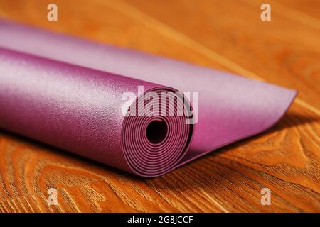A lilac-colored yoga mat is spread out in a roll on the wooden floor. Close-up Stock Photo