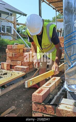 A brick layer constructs the external wall of a new bungalow in Surrey, UK. Shows scaffolding loaded out with traditional clay bricks. Stock Photo