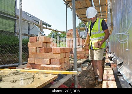 A brick layer constructs the external wall of a new bungalow in Surrey, UK. Shows scaffolding loaded out with traditional clay bricks. Stock Photo