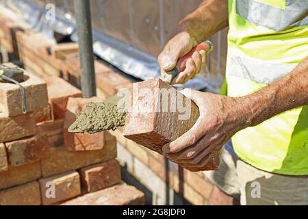 Close-up of a brick layer constructing the external wall for a new bungalow in Surrey, UK. Shows 'buttering' the brick end with mortar before laying. Stock Photo