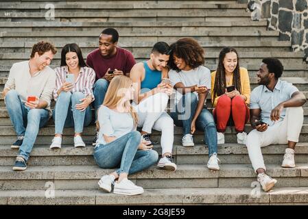 Multiethnic friends sitting on steps and using smartphones Stock Photo