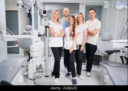 Team of professional dentists and assistants looking at camera and smiling while posing in modern dental office. Dream team. Dentistry and medicine co Stock Photo