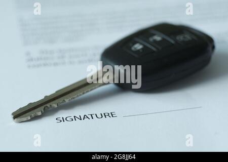 There is a contract and car keys on the table, the emphasis is on keys and signatures. Blurred image. Stock Photo