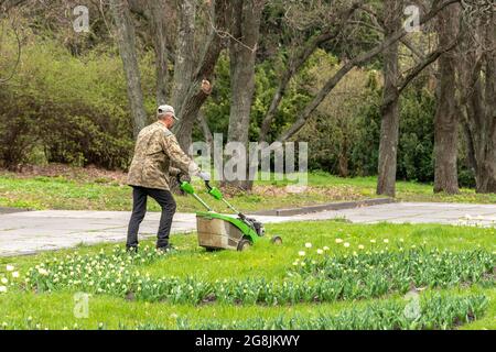 Kiev, Ukraine - April 27, 2021: A man with a lawn mower mows the grass in the park. Stock Photo