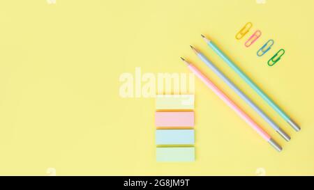 office supplies on a yellow background with copy space. Graphite pencils, paper clips and sticky notes Stock Photo