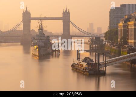 City of London, UK. 21st July, 2021. UK Weather: Beautiful hazy sunrise over Tower Bridge, The City of London and HMS Belfast as the capital wakes up to another day of glorious sunshine and clear skies during the heatwave. Credit: Celia McMahon/Alamy Live News Stock Photo