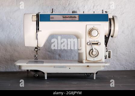 Vintage retro sewing machine from 60s or 70s on wooden table with white wall background. Stock Photo