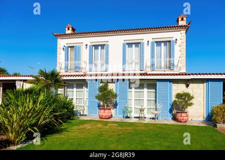 Aegean or Mediterranean type luxury stone villa exterior with blue shutters and garden. Stock Photo
