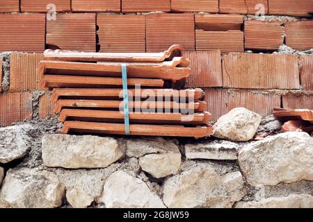 Stack of roof tiles on a stone garden wall with red brick background. Stock Photo