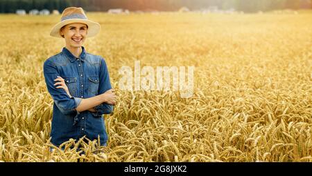 smiling young female farmer standing with arms crossed in wheat cereal field. copy space Stock Photo