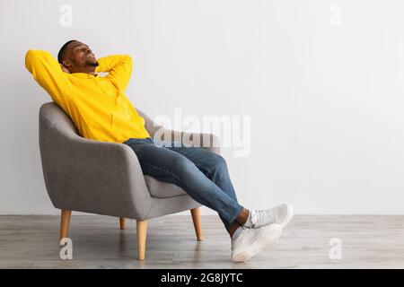 Black Guy Relaxing Sitting In Comfortable Chair Over Gray Wall Stock Photo