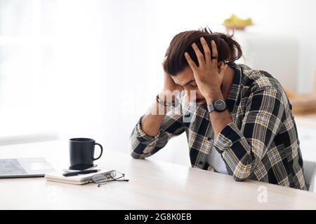 Depressed arab man sitting at worktable, touching his head Stock Photo