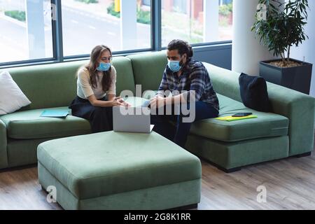 Two diverse creative colleagues wearing face masks talking at meeting Stock Photo