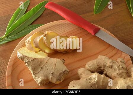 Ginger root slice on wooden cutting board  on wooden table with leaves. Top elevated view. Stock Photo