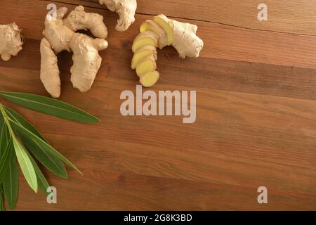 Ginger root as a product for healing purposes with sliced portions and leaves on wooden table. Top view. Stock Photo