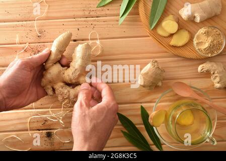 Organic ginger infusion on wooden table in the countryside and hands with roots ginger. Top view. Stock Photo