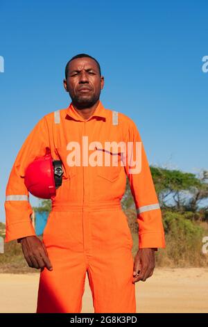 Concept of engineer or technician. Male mechanic in orange uniform with helmet on his arm. Stock Photo