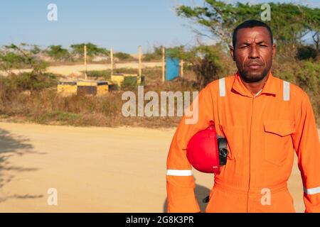 Concept of engineer or technician. African male mechanic in orange uniform with helmet on his arm. Stock Photo