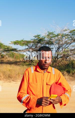 Male mechanic checking his cell phone with helmet on his arm. Concept of engineer or technician. Stock Photo