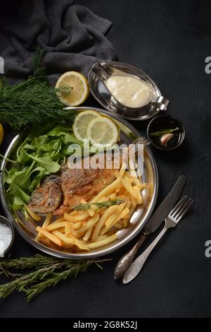 Fried fish dorado with potatoes chips, fresh herbs and lemon Stock Photo