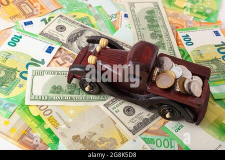 wooden car with coins on euro and dollars texture background Stock Photo